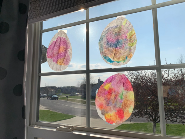 Watercolor and coffee filter Easter eggs hang in the window, waiting to be found on a contactless Easter egg hunt.