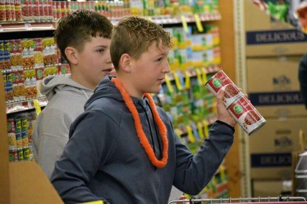 Reid Robinson holds up cans of beans during the middle school’s Hunger Games event Friday morning at Gene’s Heartland Foods.
 